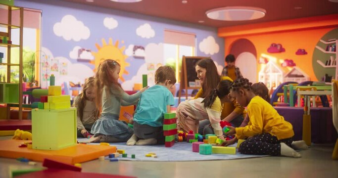 Creative Multiethnic Friends Playing in Kindergarten Together with Female Pedagogue. Boys and Girls Constructing a House Out of Colorful Building Blocks. Children Having Fun in Modern Daycare Center