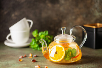 Glass teapot with hot citrus tea from oranges, lemons, apples and mint. Healthy drink on  dark...