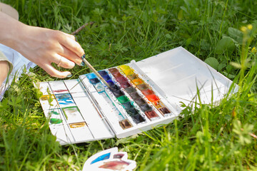 Brush in hand and watercolor palette, woman drawing and painting on plein air in the summer park on...