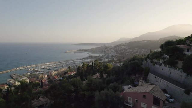 Menton village in the Cote D'azur Mediterranean south coast of France during sunset with homes and ramparts, Aerial flyover shot