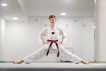 Taekwondo boy with spread legs wearing kimono and posing at martial art school.