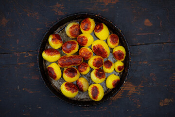 an old rustic frying pan with whole small potatoes fried in vegetable oil on a black wooden table top view
