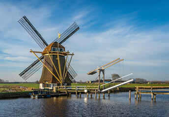 Obraz premium Scenery with wooden drawbridge and historical windmill in dutch village of Baambrugge