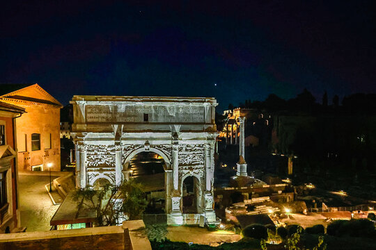 Italy, Rome - November 26, 2023: Roman Forum Illuminated at night. Architecture of ancient Rome. View from Capitoline Hill on temple of Saturn, Triumphal Arch of Septimius Severus, Italy