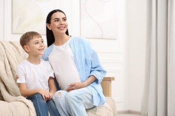 Obraz premium Happy pregnant woman with her son on sofa at home, space for text