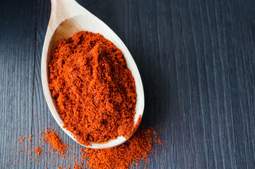 Red paprika powder in a wooden spoon. Dark background, close up, selective focus