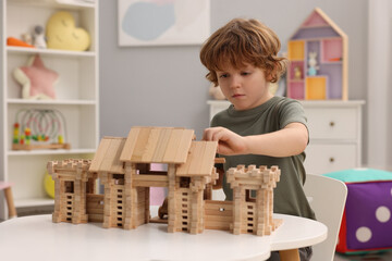Little boy playing with wooden entry gate at white table in room. Child's toy