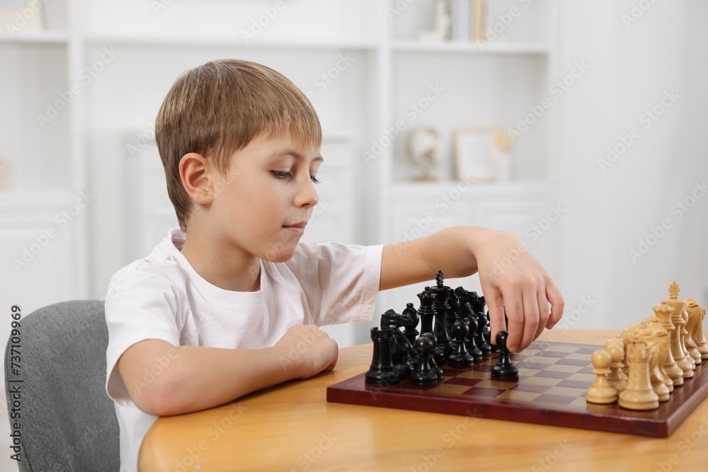 Sticker Cute little boy playing chess at table in room