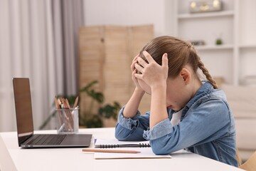 Little girl suffering from headache while doing homework at home