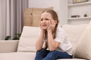 Fototapeta premium Little girl suffering from headache on sofa indoors