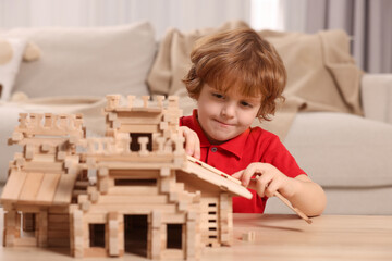 Cute little boy playing with wooden castle at table in room. Child's toy