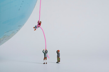 Photography of miniature people and toy figures, A mountaineer climbs up a globe on a rope and is...