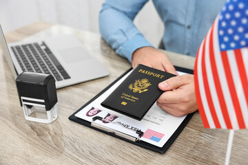 Immigration to United States of America. Man with passport and visa application form at wooden table in office, closeup