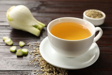 Fennel tea in cup, seeds and fresh vegetable on wooden table, closeup