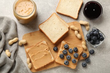 Tasty peanut butter sandwiches with fresh blueberries and jam on gray table, flat lay