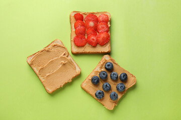 Tasty peanut butter sandwiches with fresh berries on light green background, flat lay