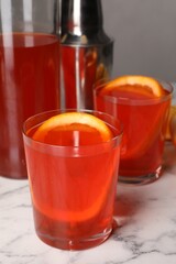 Aperol spritz cocktail and orange slices in glasses on white marble table, closeup