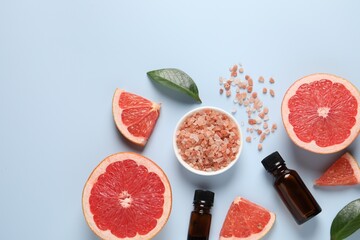 Grapefruit essential oil in bottles, sea salt and cut fruit on light blue table, flat lay. Space for text