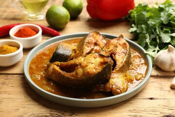 Tasty fish curry and ingredients on wooden table, closeup. Indian cuisine
