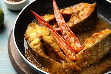 Tasty fish curry in frying pan on light blue table, closeup. Indian cuisine