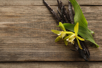 Vanilla pods, beautiful flowers and green leaves on wooden table. Space for text