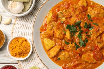 Delicious chicken curry and ingredients on wooden table, flat lay