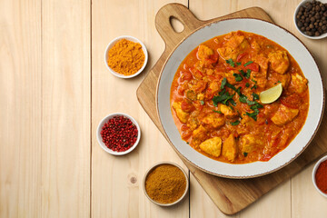Delicious chicken curry and spices on wooden table, flat lay. Space for text
