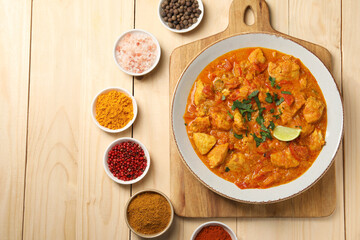 Delicious chicken curry and spices on wooden table, flat lay. Space for text