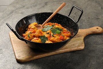Delicious chicken curry in frying pan and spoon on grey table