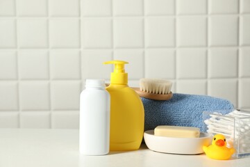 Baby cosmetic products, bath duck, cotton swabs and towel on white table against tiled wall. Space...