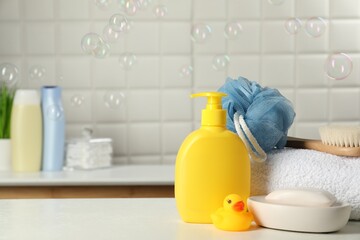 Baby cosmetic products, bath duck, brush and towel on white table against soap bubbles. Space for...