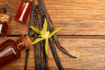 Aromatic vanilla extract, pods and flower on wooden table, flat lay. Space for text