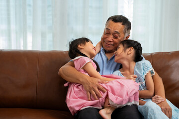 Happy Asian senior grandfather sits on a couch with his granddaughter and plays with his granddaughter in the living room at home, The Concept of family having fun in their house