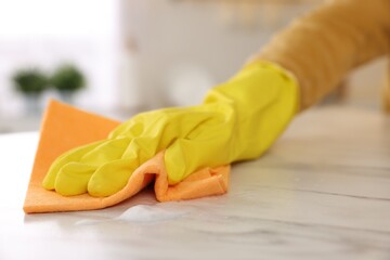 Woman with microfiber cloth cleaning white marble table in kitchen, closeup