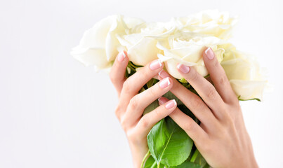 Hands of a woman with beautiful french manicure and bouquet of white roses