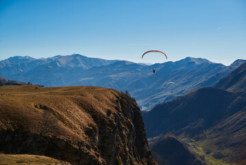 Drifting peacefully in the pure sky, the paraglider glides next to the majestic brown mountain...
