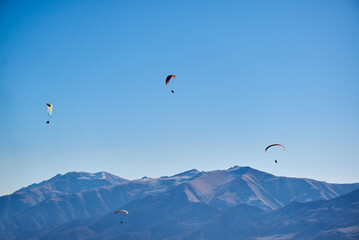 Drifting easily in the clear sky, paragliders admire the majestic brown mountain peaks.