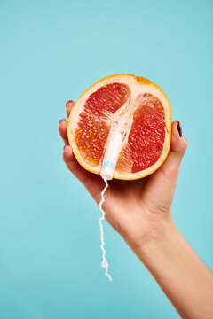 object photo of fresh juicy grapefruit with tampon in it in hand of unknown woman on blue backdrop