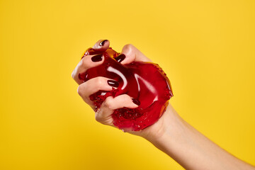 unknown young woman with nail polish squeezing red delicious jello in her hand on yellow background - 737142141