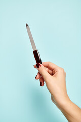 object photo of nail file in hand of young unknown woman with nail polish on blue background