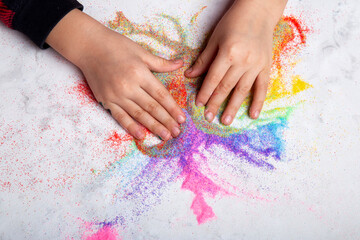 Child hands playing with rainbow colored sand. Motor skills, child creativity concept