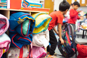 Blurry background students in pre-k school with full storage cabinet of rolled toddler nap mats,...