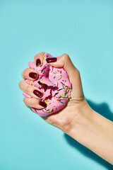unknown female model with nail polish squeezing pink sweet donut on blue vibrant background