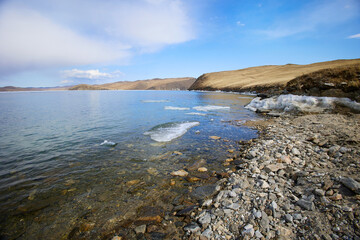 Lake Baikal in spring. Ice floes in the lake, ice melting time, clear water, pebble beach.