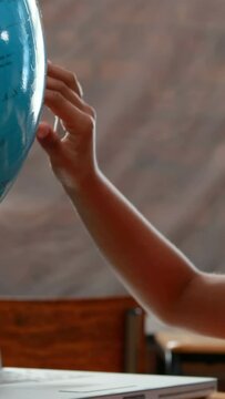 Vertical video of a child's hand touching a globe in a classroom setting