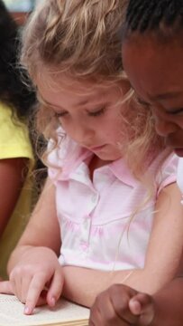 Vertical video of Caucasian and African American girls reading together at school