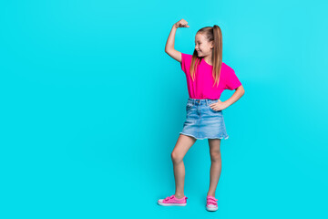 Full length photo of adorable lovely girl in trendy clothes showing muscular arm standing empty space isolated on cyan color background