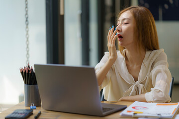 Young Asian businesswoman yawning while working with laptop computer at the office, woman in casual...