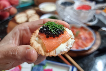 Finger holding cracker topped with expensive black caviar on smoked salmon and dill