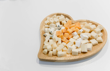 A variety of cheese on a wooden plate in the shape of a heart. 